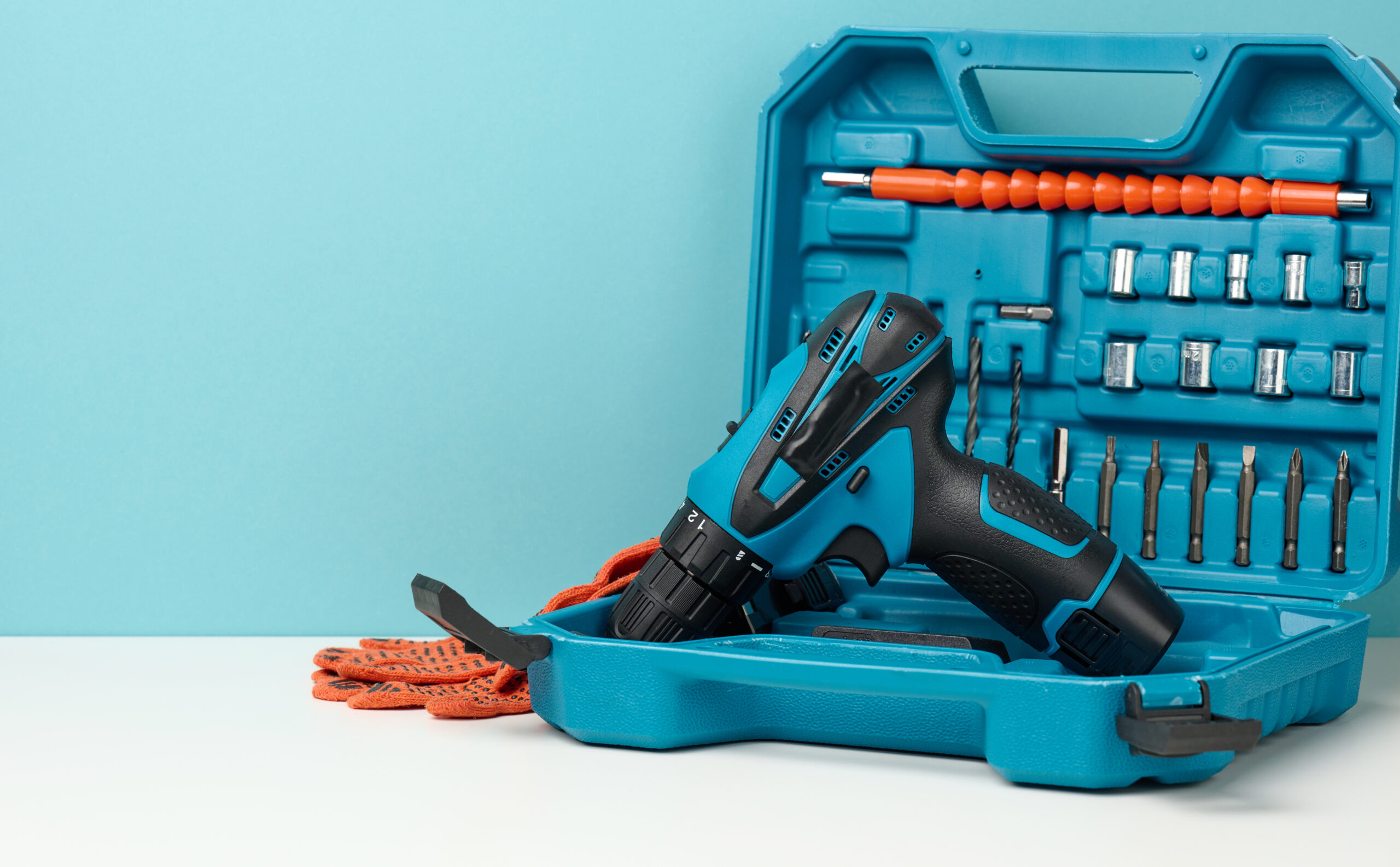 plastic box with cordless drill and set of drills and screwdrivers on white background, copy space
